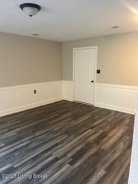 spare room featuring dark wood-style floors, visible vents, and wainscoting