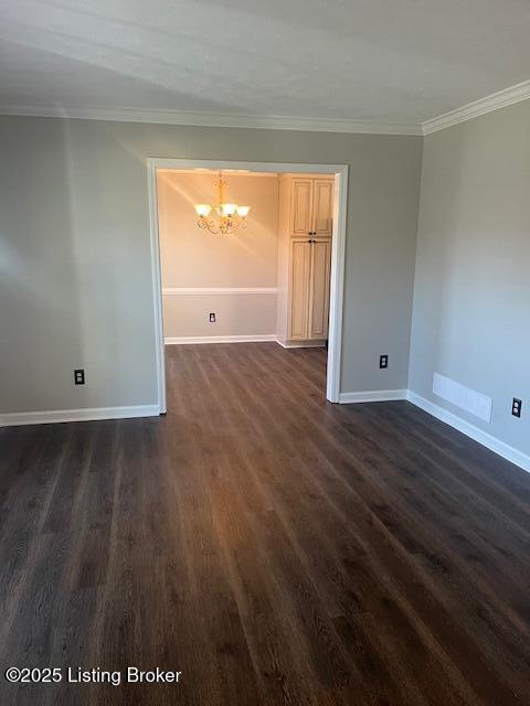 empty room featuring dark wood-style floors, a notable chandelier, crown molding, and baseboards