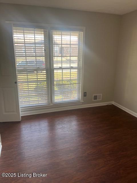 empty room with dark wood-type flooring, visible vents, and baseboards