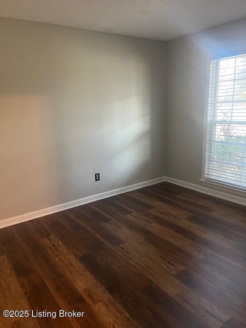 spare room with baseboards and dark wood-style floors