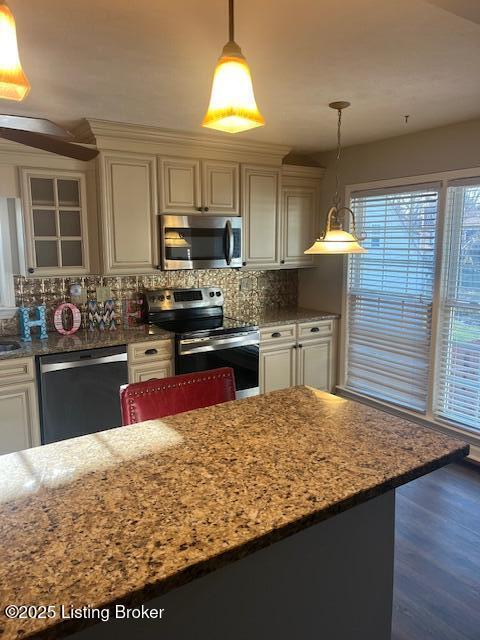 kitchen featuring backsplash, dark wood finished floors, stainless steel appliances, light stone countertops, and hanging light fixtures