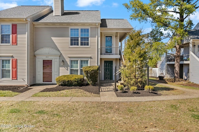 view of property with a front lawn, a balcony, roof with shingles, and a chimney