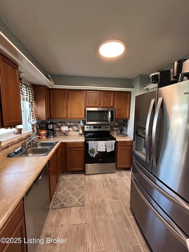 kitchen with brown cabinets, a sink, backsplash, stainless steel appliances, and light countertops