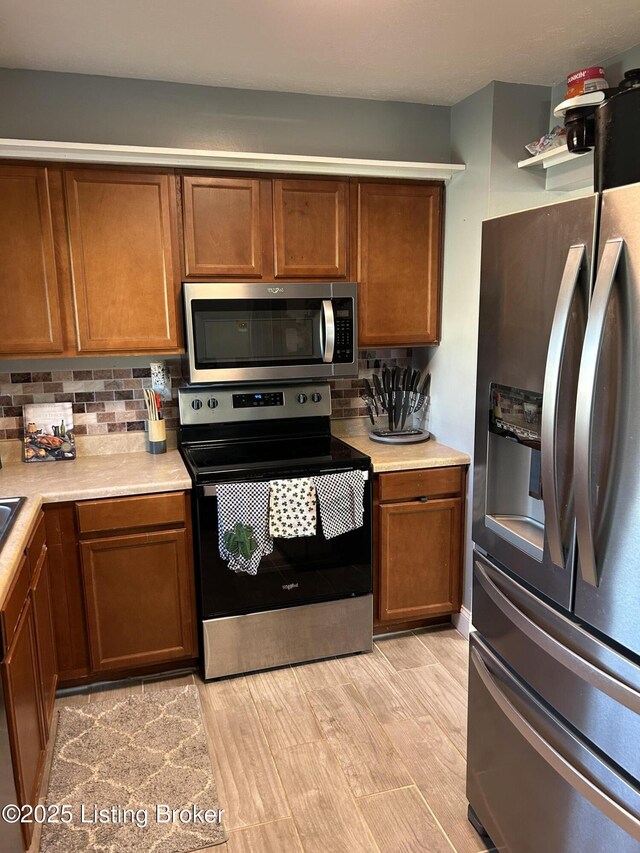 kitchen with brown cabinetry, decorative backsplash, appliances with stainless steel finishes, and light countertops