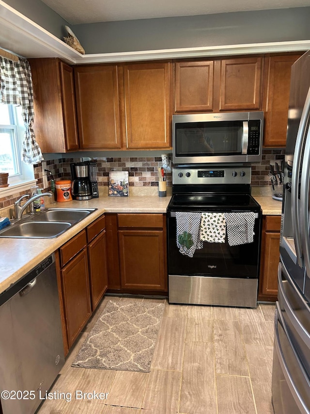 kitchen with a sink, tasteful backsplash, appliances with stainless steel finishes, brown cabinetry, and light countertops