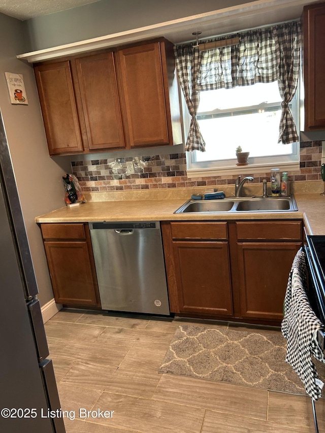 kitchen with backsplash, light countertops, appliances with stainless steel finishes, brown cabinetry, and a sink