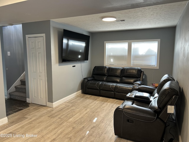 living room with stairway, baseboards, visible vents, light wood-style flooring, and a textured ceiling