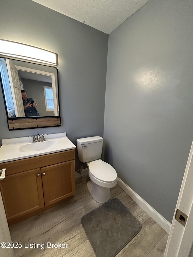 bathroom with toilet, a textured ceiling, wood finished floors, baseboards, and vanity