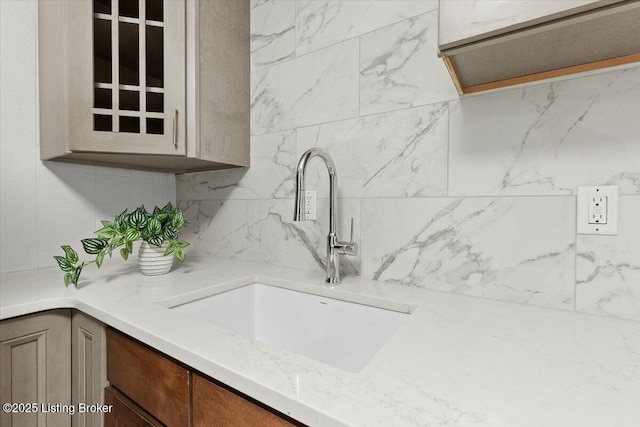 kitchen featuring decorative backsplash, glass insert cabinets, and a sink