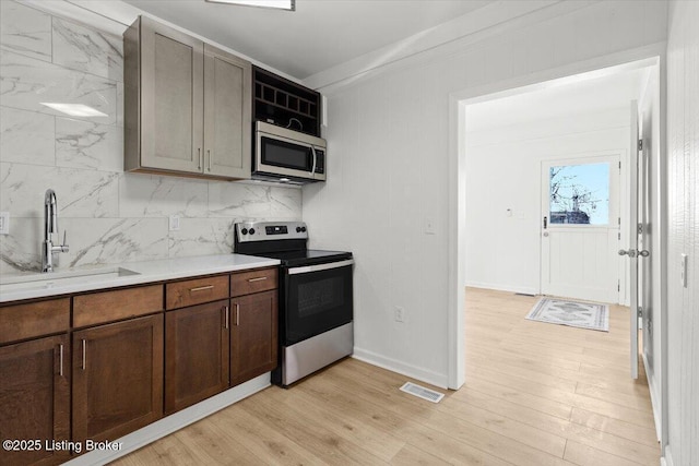 kitchen with decorative backsplash, appliances with stainless steel finishes, light wood-type flooring, and a sink