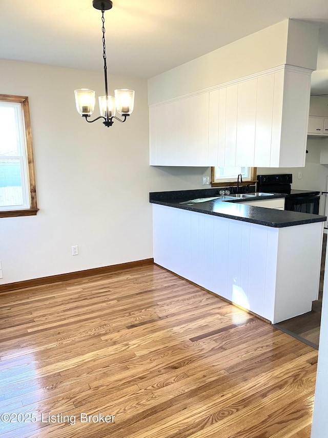 kitchen featuring light wood finished floors, electric range, white cabinetry, dark countertops, and a notable chandelier