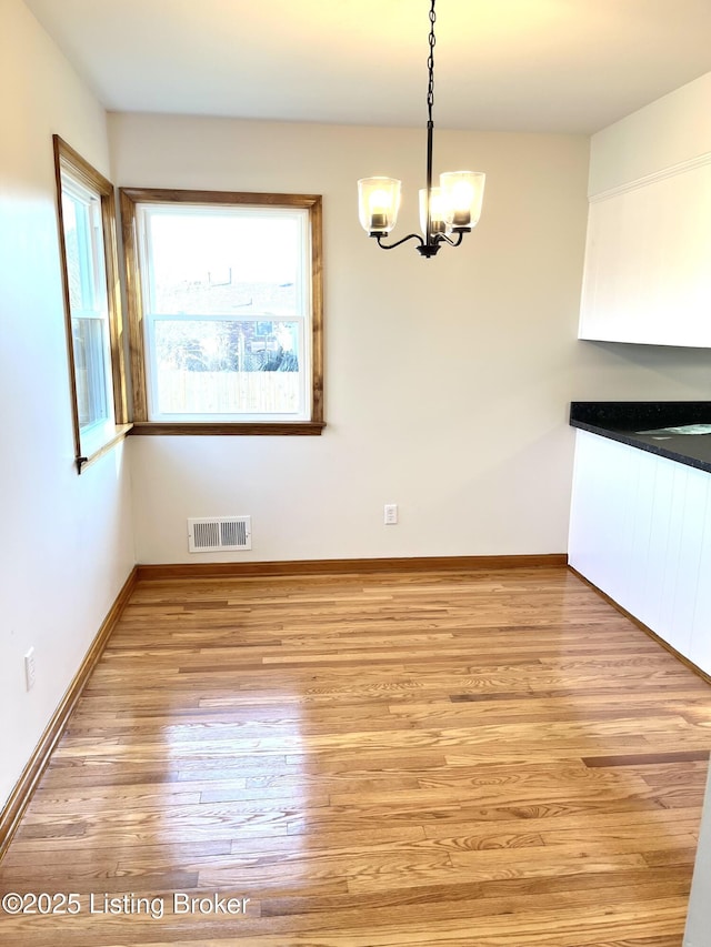 unfurnished dining area with a chandelier, visible vents, light wood-type flooring, and baseboards