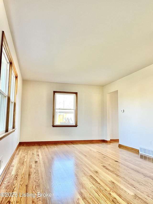 unfurnished room featuring light wood-style floors, visible vents, and baseboards