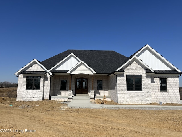 view of front facade featuring a standing seam roof, french doors, stone siding, brick siding, and metal roof