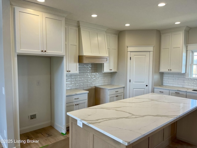 kitchen with light stone counters, light wood finished floors, custom exhaust hood, white cabinets, and a center island