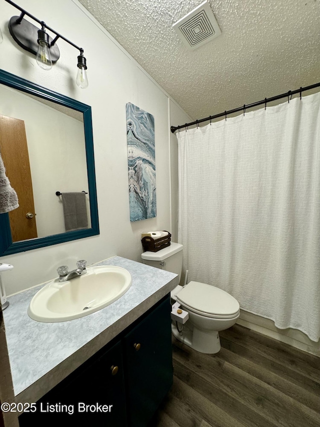 full bathroom featuring visible vents, toilet, vanity, wood finished floors, and a textured ceiling