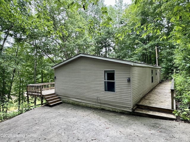 view of property exterior with a deck, a wooded view, and a patio area