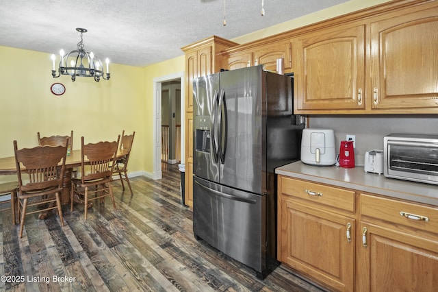 kitchen featuring a notable chandelier, a textured ceiling, stainless steel fridge, a toaster, and dark wood-style flooring