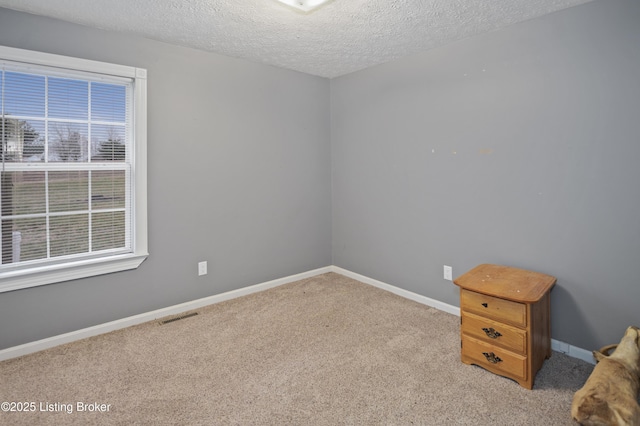 carpeted empty room with baseboards, visible vents, and a textured ceiling