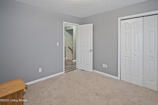 unfurnished bedroom featuring carpet flooring, baseboards, a closet, and a textured ceiling