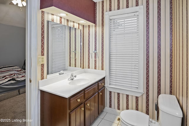 ensuite bathroom with tile patterned floors, toilet, wallpapered walls, baseboards, and vanity