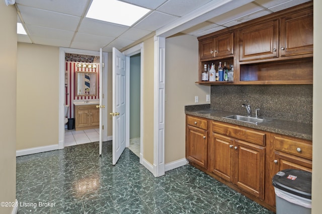 bar featuring a drop ceiling, baseboards, backsplash, and a sink