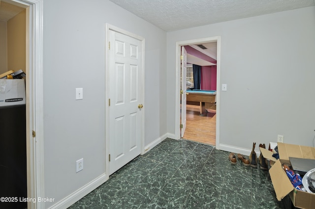 hall featuring visible vents, a textured ceiling, baseboards, and dark floors