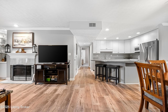 living area with a high end fireplace, visible vents, ornamental molding, light wood-style flooring, and a textured ceiling