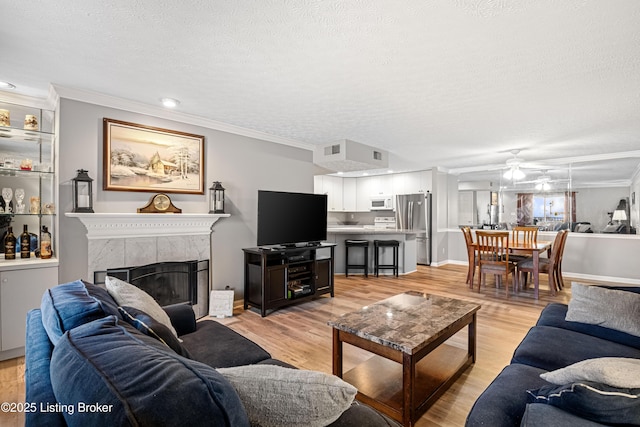 living area featuring a fireplace, a ceiling fan, light wood-style floors, and a textured ceiling