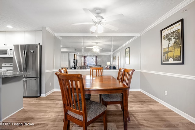 dining room featuring light wood-style flooring, ornamental molding, a textured ceiling, baseboards, and ceiling fan