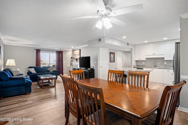 dining space with a textured ceiling, light wood-type flooring, a ceiling fan, and ornamental molding