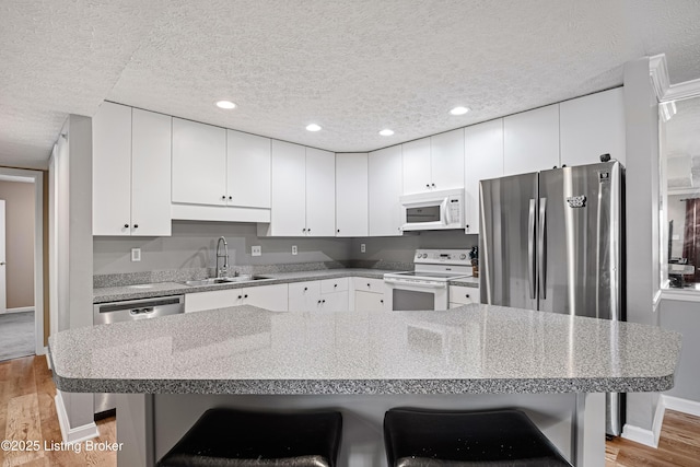 kitchen with light wood finished floors, a sink, stainless steel appliances, a textured ceiling, and a kitchen breakfast bar