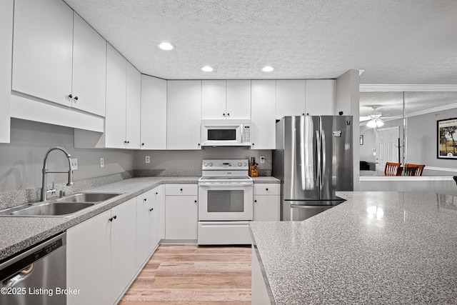 kitchen featuring light wood-style flooring, a sink, white cabinets, appliances with stainless steel finishes, and a textured ceiling