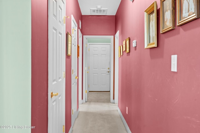 hallway with light colored carpet, visible vents, and baseboards