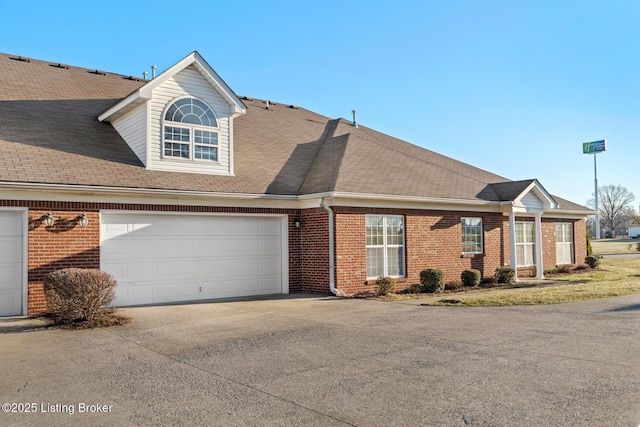 view of front of house with driveway, brick siding, roof with shingles, and an attached garage