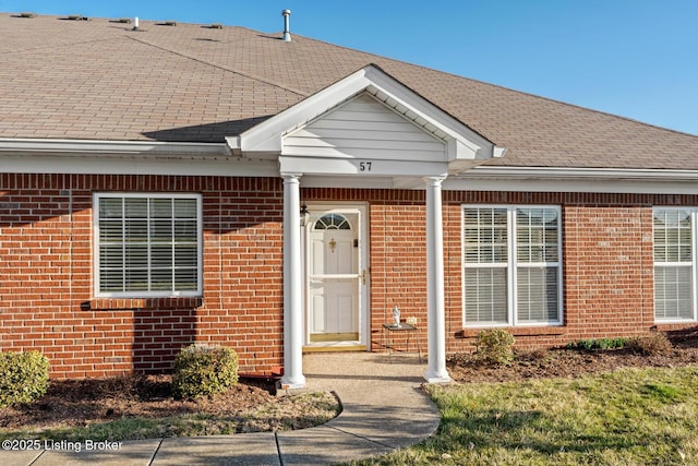 doorway to property featuring brick siding and roof with shingles