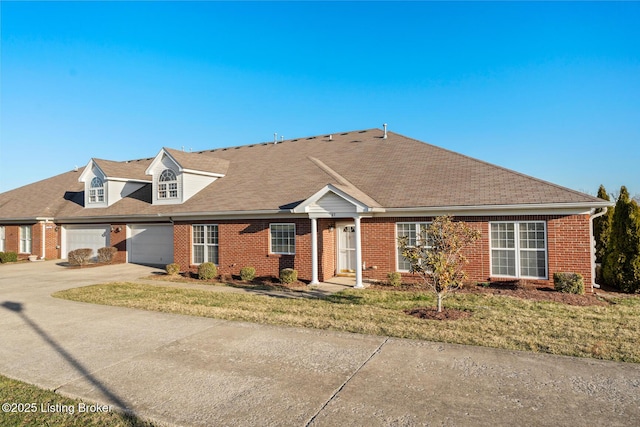 view of front facade with brick siding, concrete driveway, roof with shingles, and a front yard