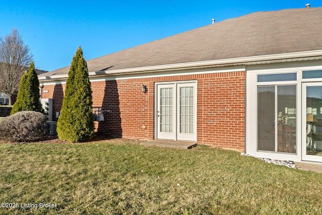 rear view of property featuring a yard, brick siding, and roof with shingles