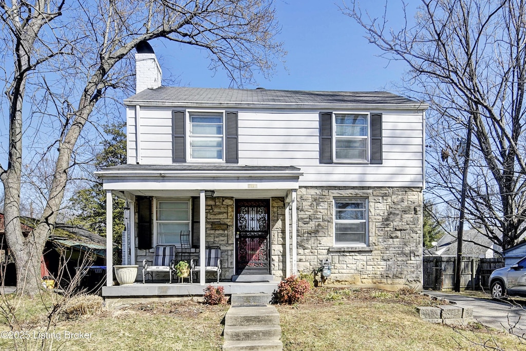 view of front facade with stone siding, covered porch, a chimney, and fence