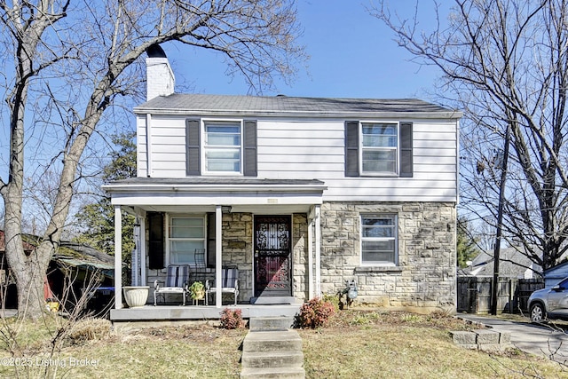 view of front facade with stone siding, covered porch, a chimney, and fence