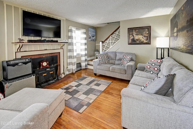 living area with a fireplace, a textured ceiling, wood finished floors, and stairs