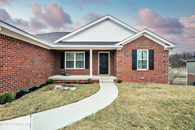 view of front of property featuring a front yard, a porch, brick siding, and a shingled roof