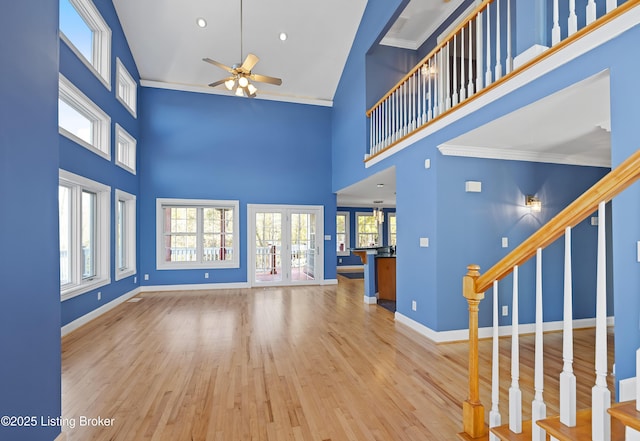 unfurnished living room with stairway, wood finished floors, baseboards, ceiling fan, and a towering ceiling