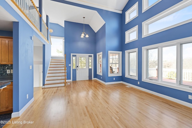 entryway with stairway, baseboards, high vaulted ceiling, and light wood-style flooring