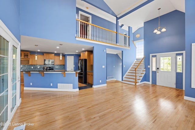 unfurnished living room with a chandelier, visible vents, light wood-style flooring, and stairway