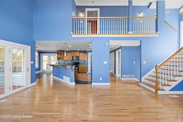 unfurnished living room with visible vents, baseboards, stairs, light wood-style flooring, and a high ceiling