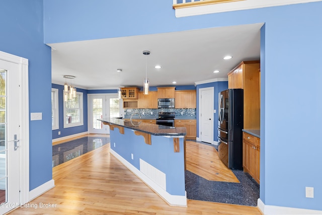 kitchen featuring a kitchen bar, a kitchen island with sink, stainless steel appliances, decorative backsplash, and baseboards