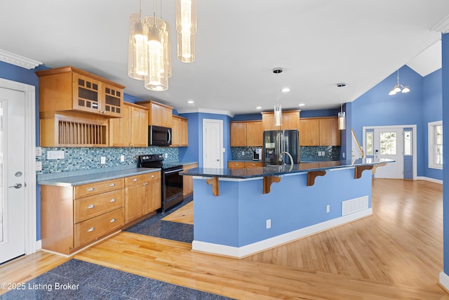 kitchen with a breakfast bar, decorative backsplash, black appliances, and light wood-type flooring