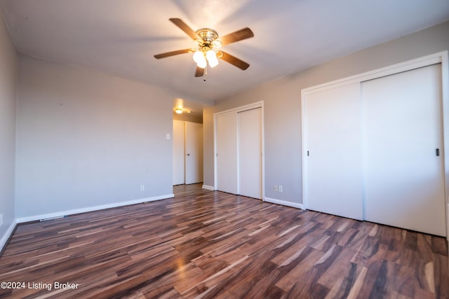 unfurnished bedroom with baseboards, two closets, wood finished floors, and a ceiling fan