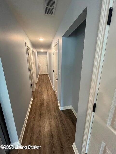 hallway featuring visible vents, baseboards, and dark wood-type flooring